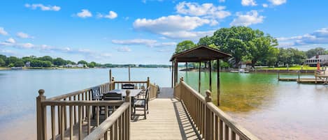 A wooden pier leading to a gazebo with a view of a lake and distant buildings.
