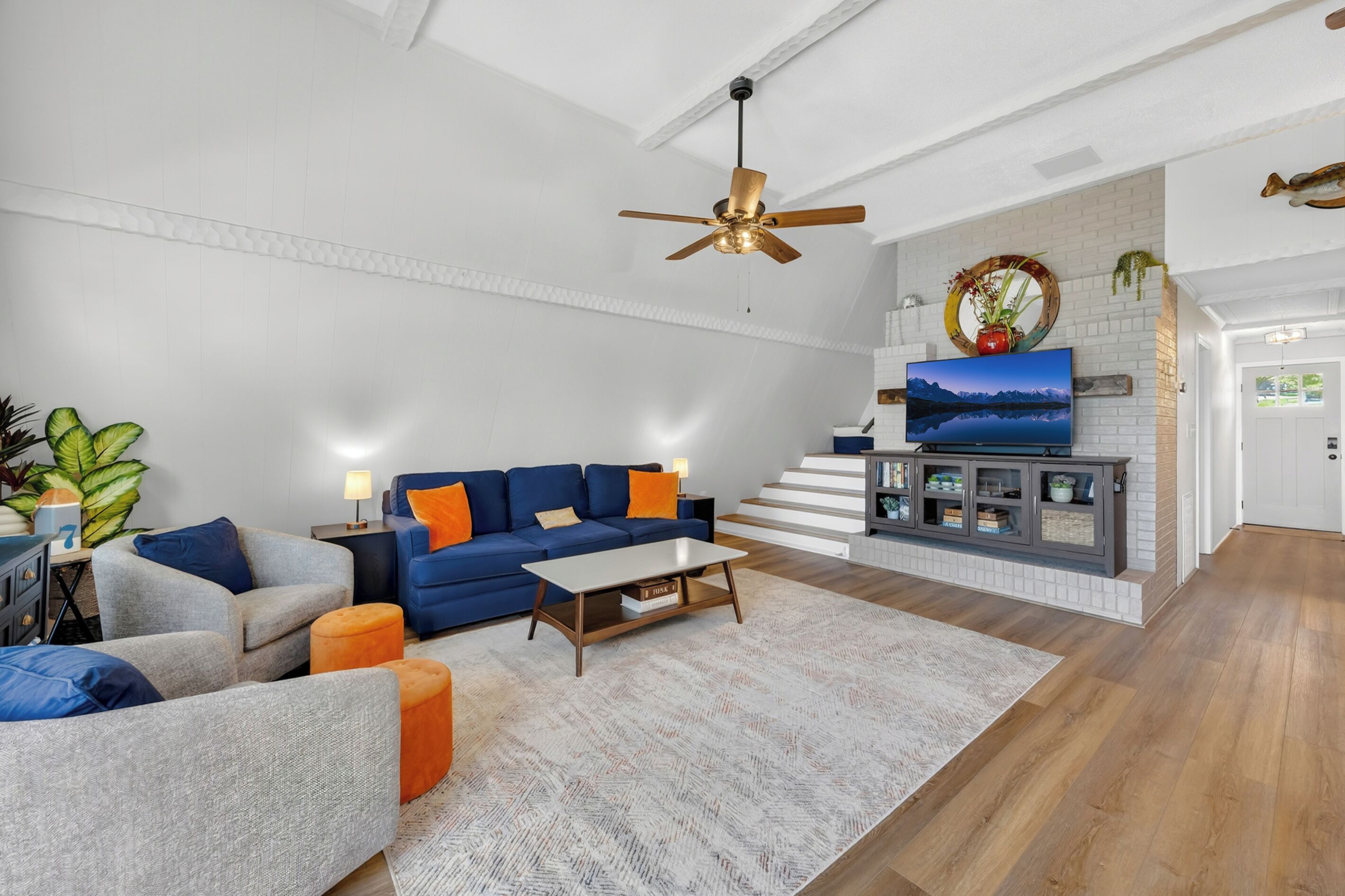 A modern living room with a blue sofa, a grey armchair, a wooden coffee table, and a TV mounted on a white brick wall.