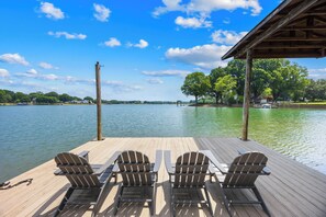 A wooden deck with three Adirondack chairs facing a calm lake, surrounded by trees and a clear sky. - Lakefront A-Frame w/ Dock, Launch + Firepit (Mooresville)