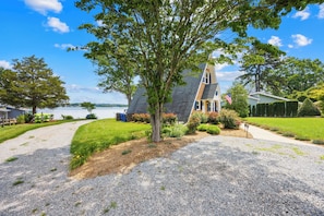 A house with a large tree in the front yard, a gravel driveway, and a view of the water. - Lakefront A-Frame w/ Dock, Launch + Firepit (Mooresville)