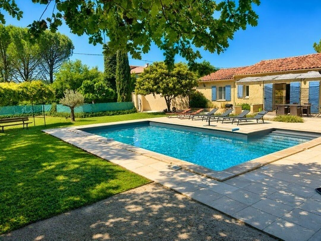Une piscine avec des chaises longues, un espace patio et un bâtiment doté d’un toit en tuiles.