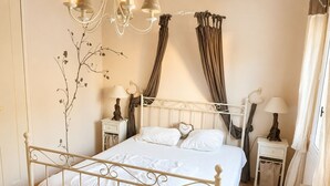 Ein Schlafzimmer mit einem weißen Metallbett, einem Chandelier, einer Wandpflanze und einem Fenster mit Vorhängen.
