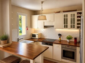 Eine moderne Küche mit weißen Schränken, einer Holz Arbeitsplatte, einer eingebauten Mikrowelle, einem Geschirrspüler und einem Backofen.