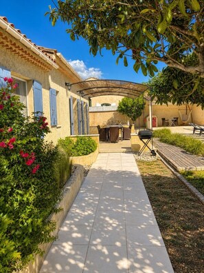 Eine Terrassenfläche mit gefliestem Weg, Gartenmöbeln und einer Pergola.