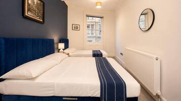 A hotel room with two beds, a window, a radiator, a framed picture, and a mirror.