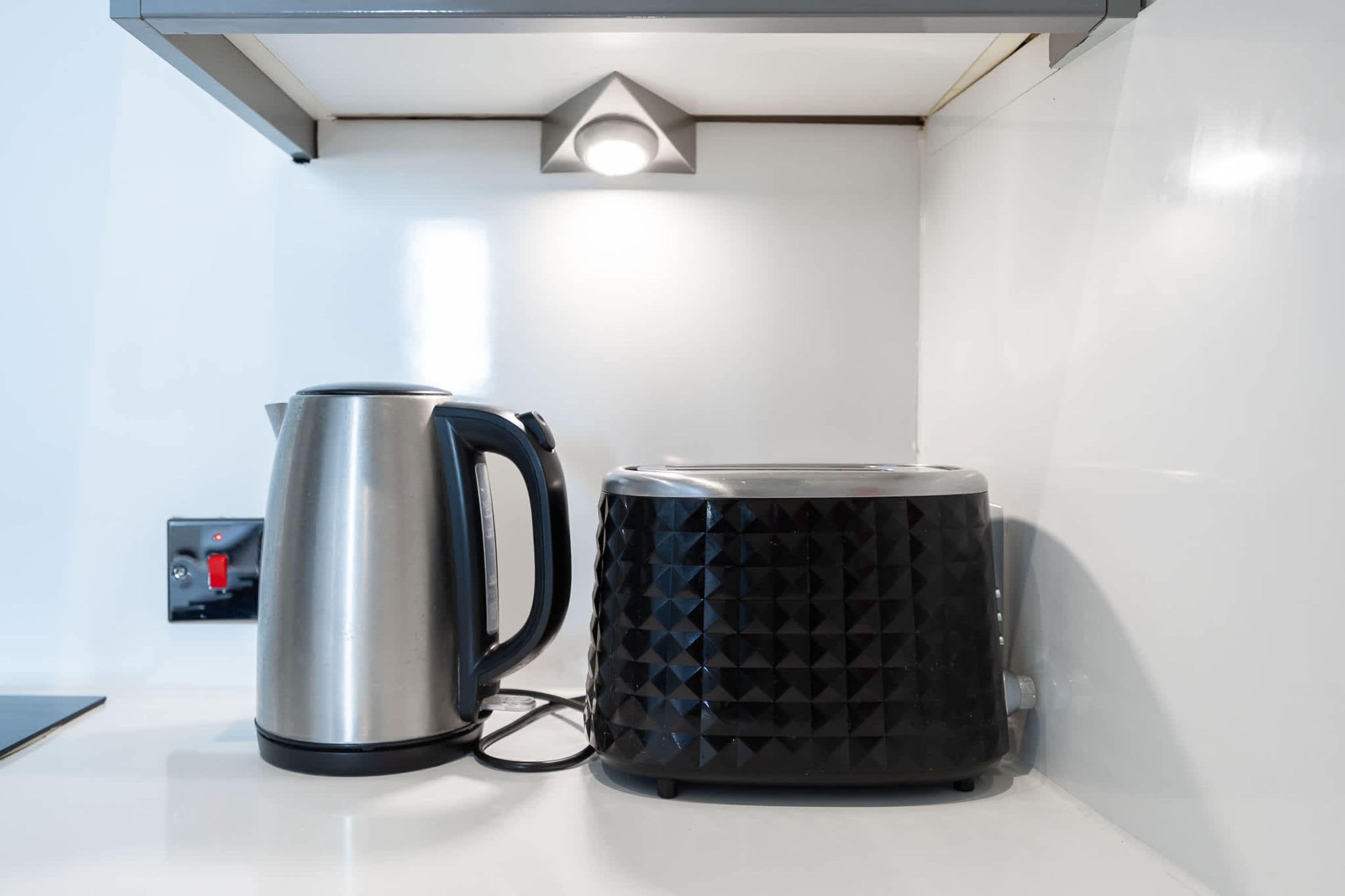 A kettle and a coffee maker on a white countertop with a light fixture above.