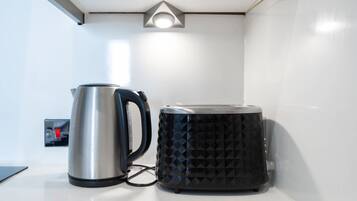 A kettle and a coffee maker on a white countertop with a light fixture above.