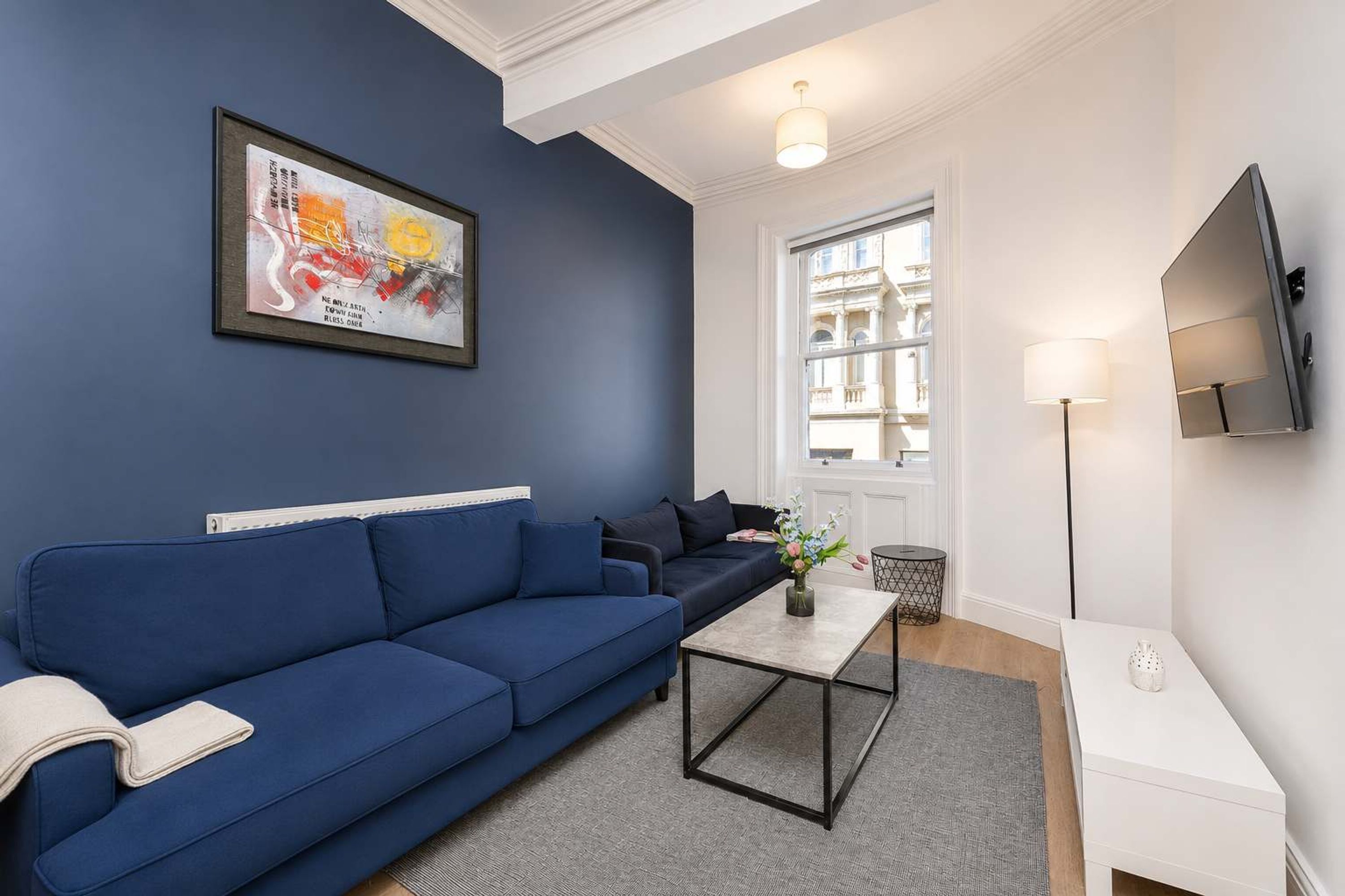 A modern living room with a blue sofa, a coffee table, a TV, and a large window.