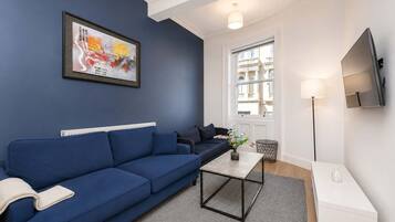 A modern living room with a blue sofa, a coffee table, a TV, and a large window.