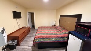 Un dormitorio con cama, televisor, escritorio, microondas y cesto de basura.