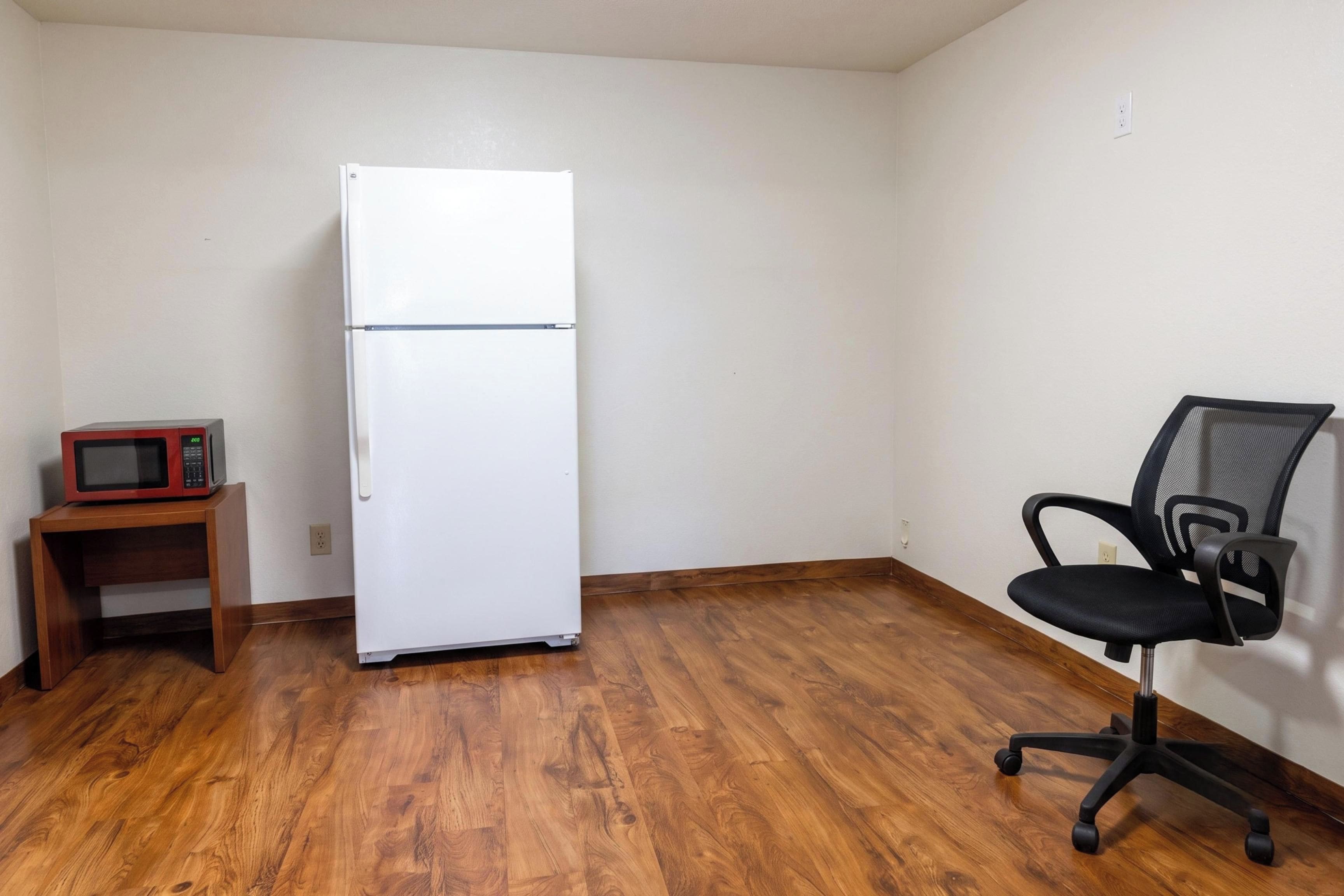 Una habitación con un refrigerador blanco, un microondas sobre una repisa de madera y una silla de oficina negra.