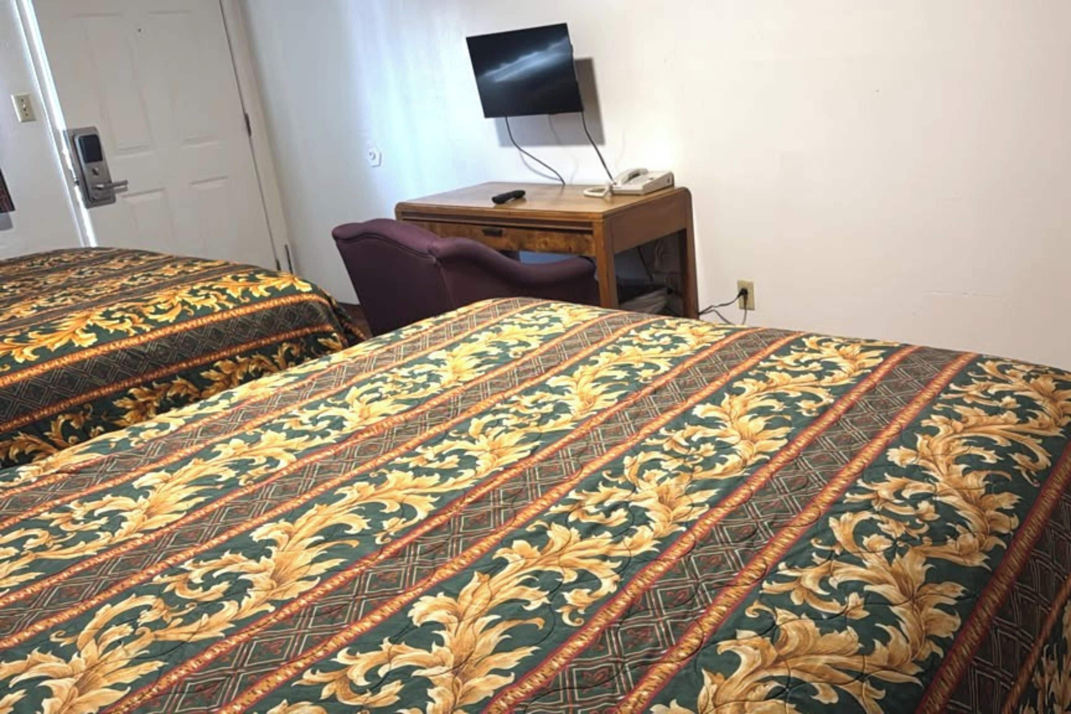 A hotel room with two beds, a desk, a chair, and a television.