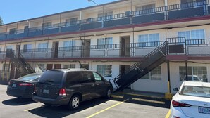 Un motel de varios pisos con estacionamiento, una escalera y un coche estacionado al frente.