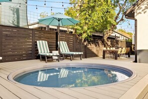 Ein Pool mit Liegestühlen und einem Sonnenschirm, umgeben von einer Holzterrasse und einer Backsteinmauer.