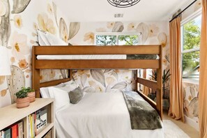 Ein Etagenbett mit Holz-Kopfteil, ein Nachttisch mit Büchern und ein Fenster mit Vorhängen.