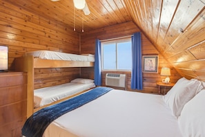 A wooden cabin room with bunk beds, a window with curtains, an air conditioning unit, and a bedside table with a lamp. - Chalet #12 Walk to Beach & Resort Amenities (Stevensville)