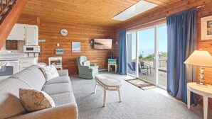 Une pièce confortable, aménagée comme un chalet, avec un plafond en bois, un canapé, un fauteuil, une petite table et une vue à travers la porte vitrée.