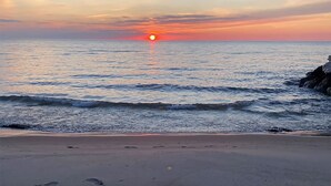 Une plage où l’on voit des empreintes de pas menant à l’eau, un coucher de soleil en arrière-plan et une mer calme.