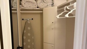 Ett litet, välordnat städskåp med en klädstång, en hopfällbar strykbräda och en dörr med ett handtag.