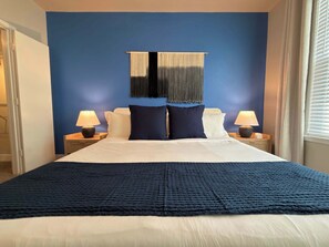 Ein Hotelzimmer mit einem großen Bett, zwei Nachttischen mit Lampen, einer blauen Akzentwand und einem Wandteppich.