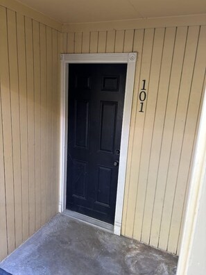 Eine beigefarbene Holztür mit einer schwarzen Platte, einem weißen Türrahmen und der Nummer 101 an der Wand.