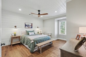 Ein Schlafzimmer mit einem Bett, Nachttischen, einer Bank, einem Deckenventilator und einem Fenster.