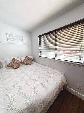 A bedroom with a bed, two pillows, a window with blinds, and a wall-mounted shelf with pictures. - Cozy Downtown Vibe Near Everything Austin (Austin)