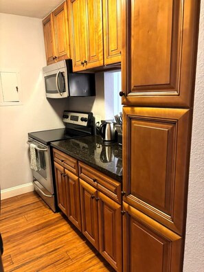 A kitchen with wooden cabinets, a microwave, a stove, and a countertop with various kitchen items. - Cozy Downtown Vibe Near Everything Austin (Austin)