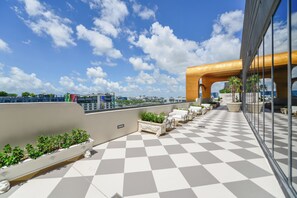 Eine Dachterrasse mit Schachbrettmuster-Boden, Sitzgelegenheiten im Freien, Pflanzgefäßen und Blick auf die Stadtlandschaft.