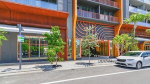 Een modern gebouw met een opvallende oranje gevel, meerdere balkons en een parkeerplaats met een witte auto.