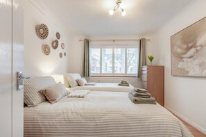A hotel room with two beds, a window with blinds, a ceiling light, and a painting on the wall. - 2 Bed in Broadstairs (oc-g34391) (Broadstairs)