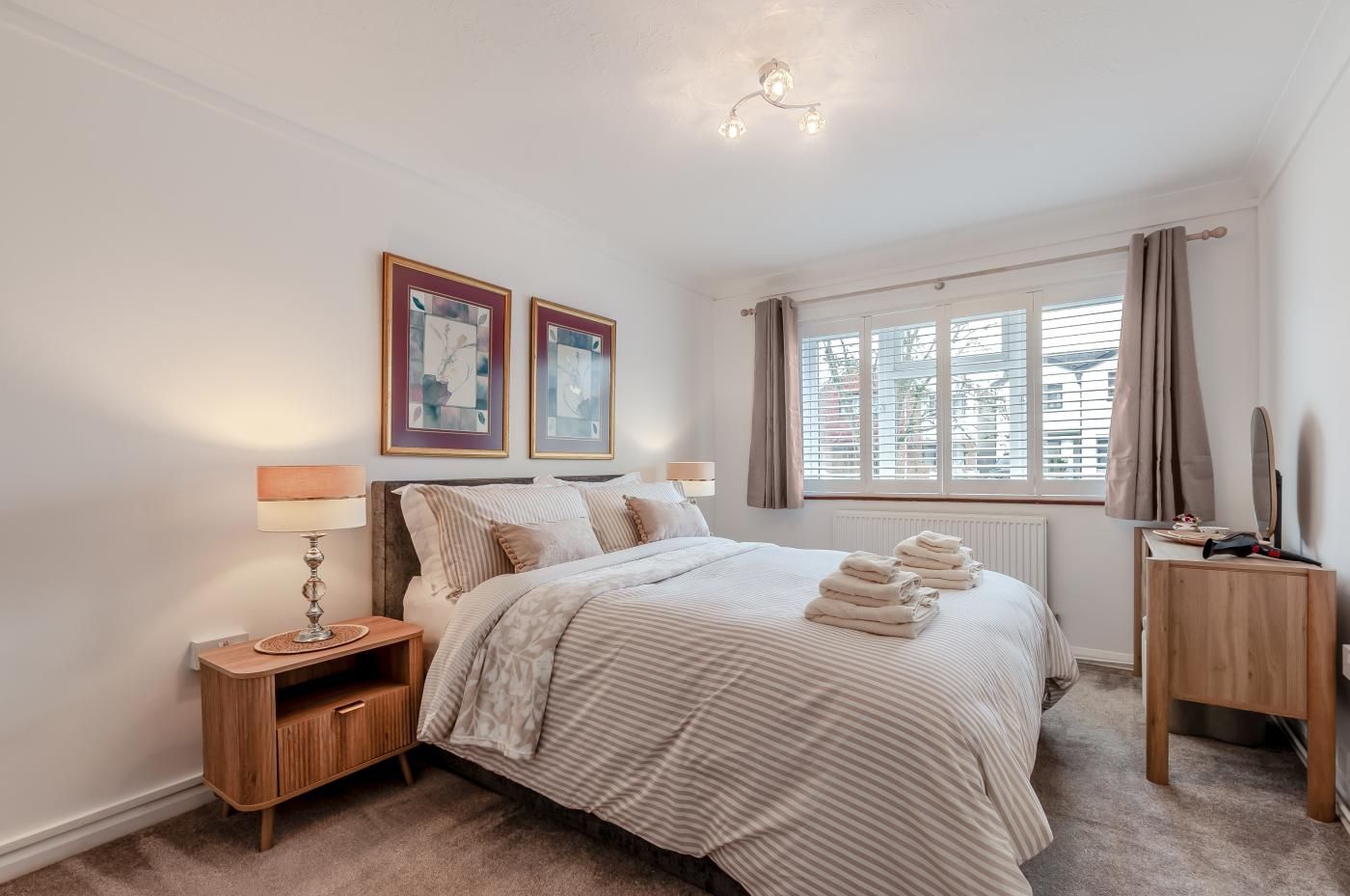 A bedroom with a bed, bedside tables, a window with curtains, and artwork on the wall.