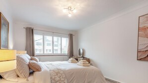 Ein Schlafzimmer mit Bett, Nachttisch, Lampe, Fenster und Kunstwerk.
