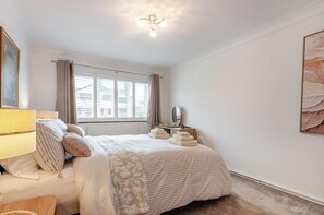 Ein Schlafzimmer mit Bett, Nachttisch, Lampe, Fenster und Kunstwerk.