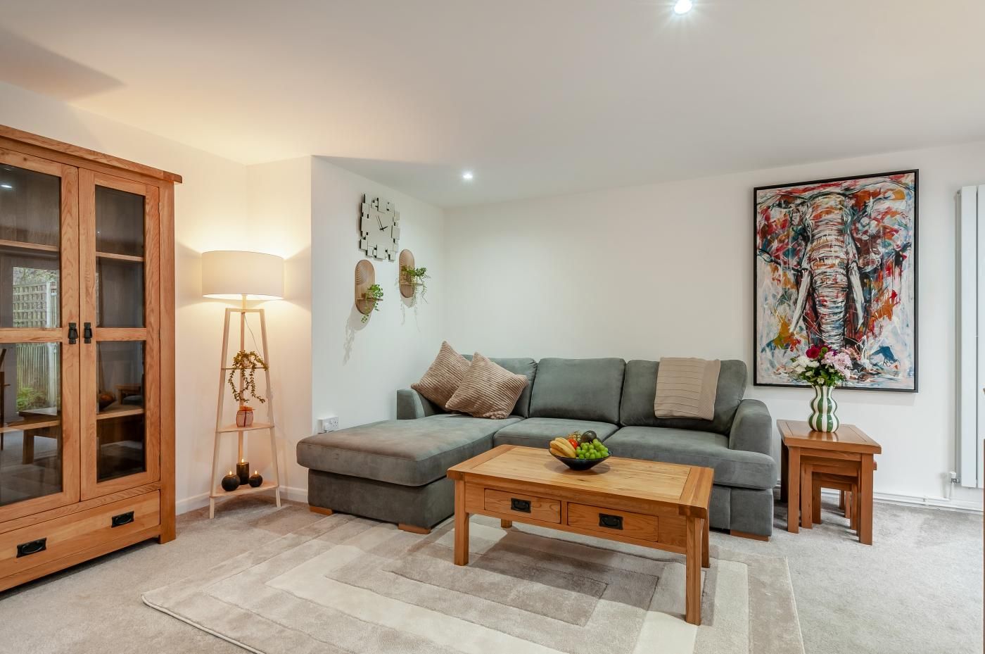 A modern living room with a grey sofa, a wooden coffee table, a cabinet with glass doors, a floor lamp, and a large abstract painting on the wall.