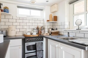 Une cuisine avec des meubles blancs, une cuisinière, un évier et une fenêtre.