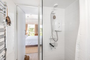 Une salle de bain moderne avec une douche, un porte-serviettes et une vue sur une chambre à coucher avec un lit et des rideaux.