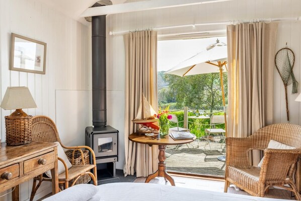 Une chambre avec un lit, une table avec une lampe, une chaise, une cheminée et une vue sur un jardin extérieur.