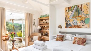 Ein Schlafzimmer mit einem Bett, einem Sessel, einem Tisch mit Lampe, einem Regal mit Dekoration und einem Bild an der Wand.
