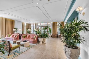 Eine geräumige Lobby mit hoher Decke, großen Fenstern und verschiedenen Sitzgelegenheiten, darunter Sofas und Sessel.