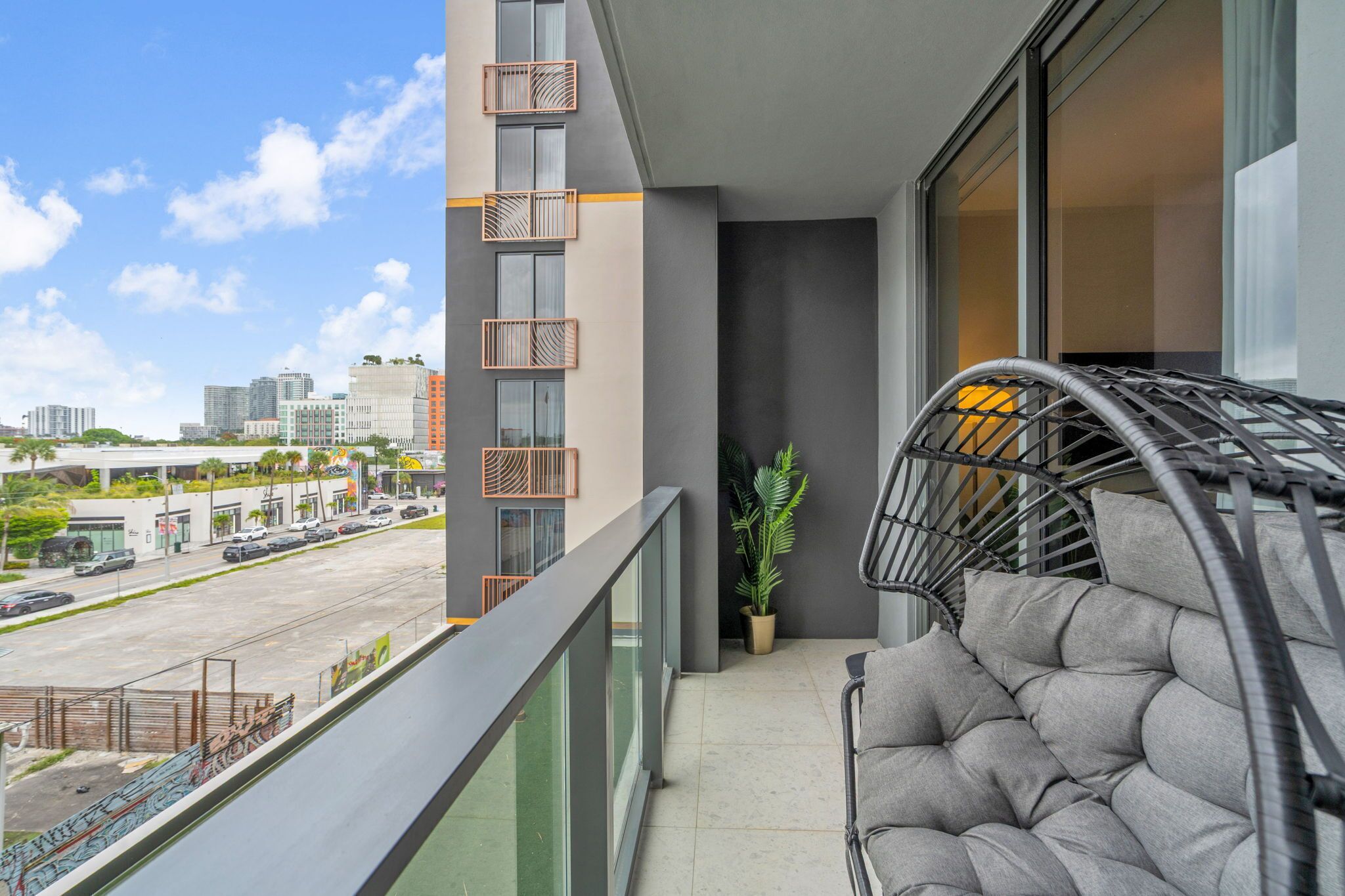 Uma varanda com uma cadeira de vime, um vaso de plantas e vista para o horizonte urbano.