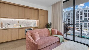 A modern kitchen with wooden cabinets, a marble countertop, and a sofa in the living area. - New Designer Condo - Rooftop Pool, Spa & Views (Miami)