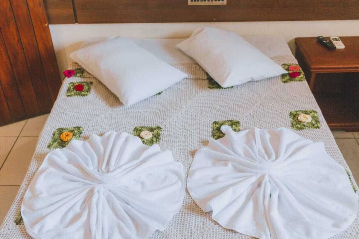 Una cama bien hecha con sábanas y almohadas blancas, un cabecero de madera y una mesita de noche con un teléfono.
