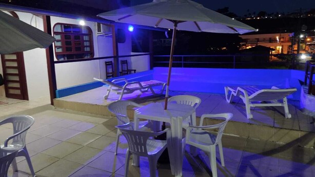 An outdoor patio with plastic chairs and tables, a white umbrella, and a railing. - HOTEL SOL BAHIA (Porto Seguro)