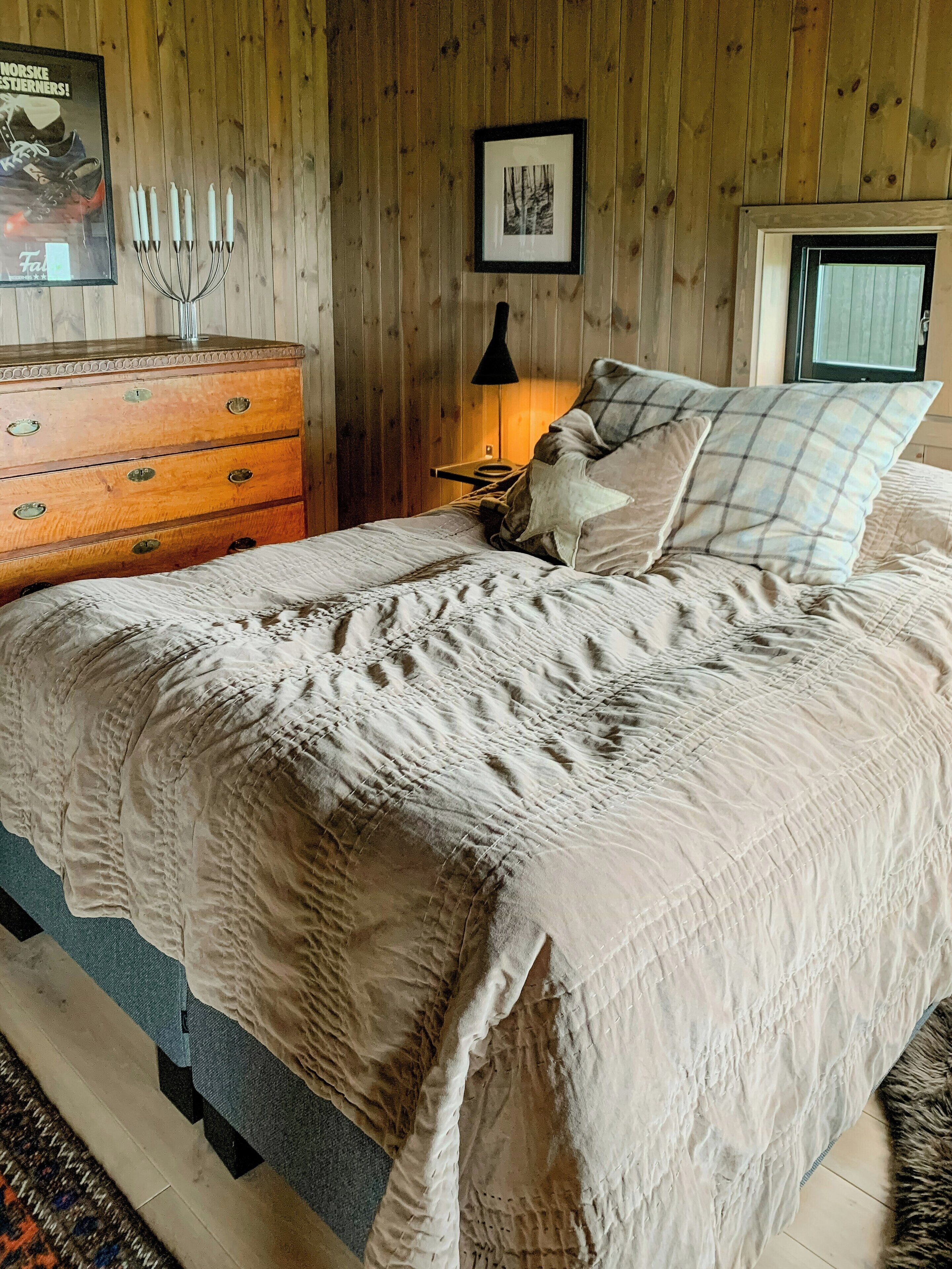 A wooden-paneled bedroom with a bed, dresser, and framed picture on the wall.