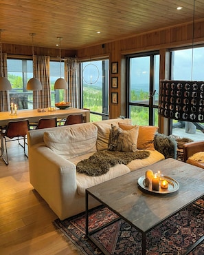 A cozy living room with a sofa, coffee table, and a dining area with a table and chairs. - Mountain cabin with panoramic view of Jotunheim (Hafjell)