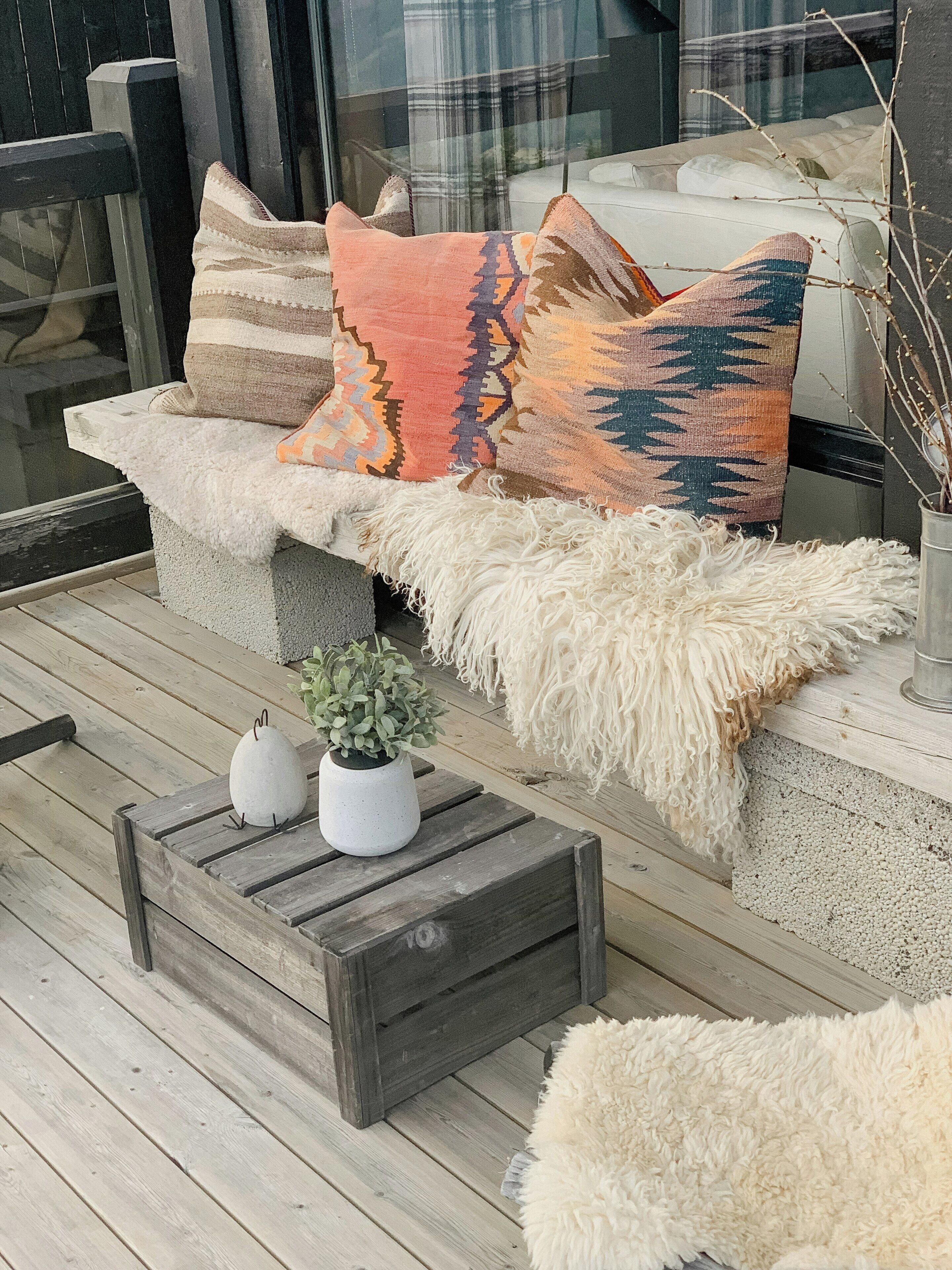 A wooden deck with a sofa, two white planters, and a fluffy white throw.
