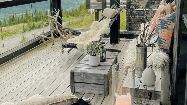 Een houten terras met een bankje, een kleine tafel en een kandelaar.
