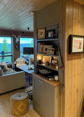 A cozy room with a wooden ceiling, a bookshelf, a fireplace, and a view of the outdoors. - Mountain cabin with panoramic view of Jotunheim (Hafjell)