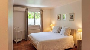 Una camera da letto con un letto, due lampade da comodino, un termosifone, una finestra con tende e un piccolo ripiano.